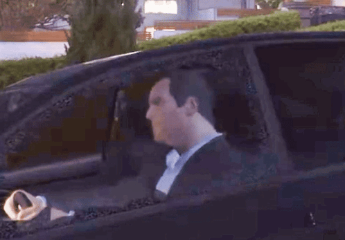 A Man In A Suit Is Driving A Car And Looking Out The Window GIF