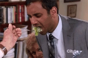 A Man In A Suit Is Eating A Piece Of Lettuce With A Fork .. GIF