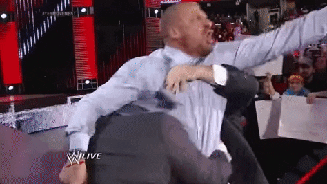 A Man In A Suit Is Fighting Another Man In A Wrestling Match On A Stage . GIF