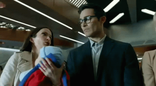 A Man In A Suit Is Holding A Baby While A Woman Holds A Baby In Her Arms . GIF