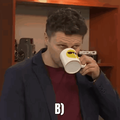 A Man In A Suit Is Holding A Coffee Mug With A Smiley Face On It And The Letter B On The Bottom GIF
