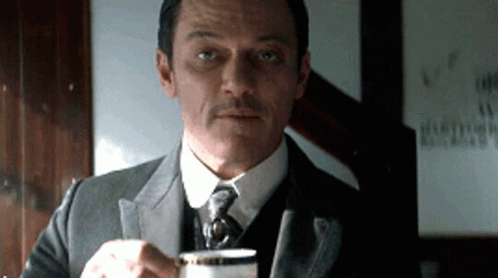 A Man In A Suit Is Holding A Cup Of Coffee GIF