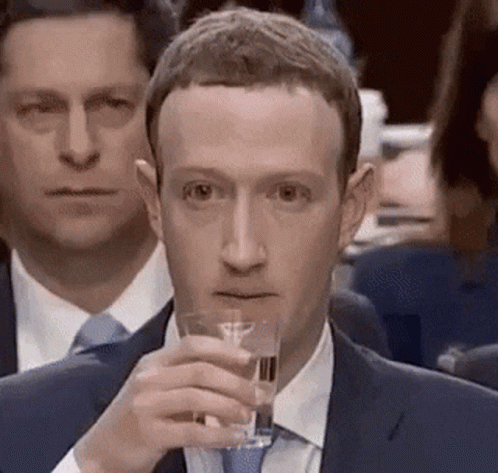 A Man In A Suit Is Holding A Glass Of Water In His Hand . GIF