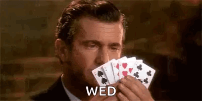 A Man In A Suit Is Holding A Hand Of Playing Cards In His Mouth . GIF