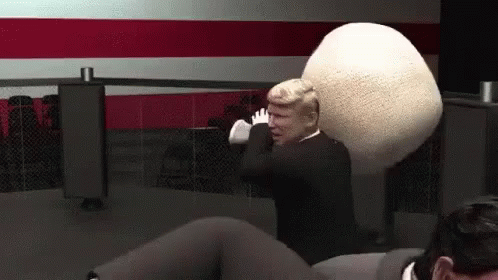 A Man In A Suit Is Holding A Large White Ball In His Hands . GIF