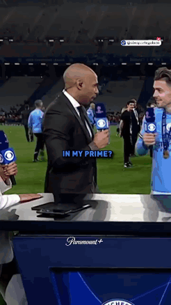 A Man In A Suit Is Holding A Microphone And Talking To Another Man In A Blue Shirt . GIF