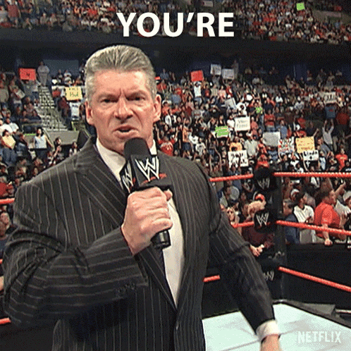 A Man In A Suit Is Holding A Microphone In Front Of A Crowd And Says You 'Re In The Background GIF