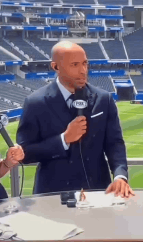A Man In A Suit Is Holding A Microphone In Front Of A Fox Stadium . GIF