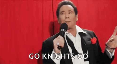 A Man In A Suit Is Holding A Microphone In Front Of A Red Curtain . GIF