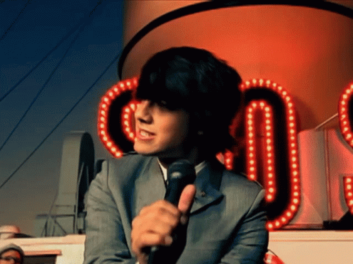 A Man In A Suit Is Holding A Microphone In Front Of A Sign That Says ' Co ' GIF