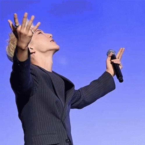 A Man In A Suit Is Holding A Microphone In His Right Hand GIF