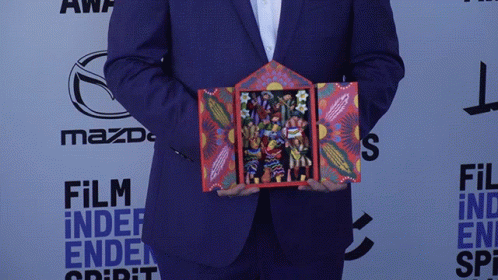 A Man In A Suit Is Holding A Painting In Front Of A Mazda Logo GIF