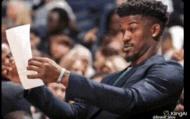 A Man In A Suit Is Holding A Piece Of Paper In His Hands . GIF