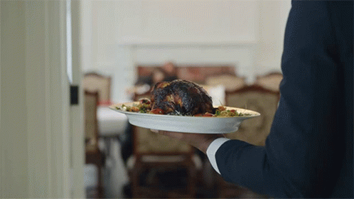 A Man In A Suit Is Holding A Plate Of Food In His Hand GIF