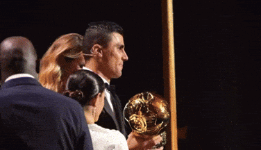 A Man In A Suit Is Holding A Trophy In His Hands GIF