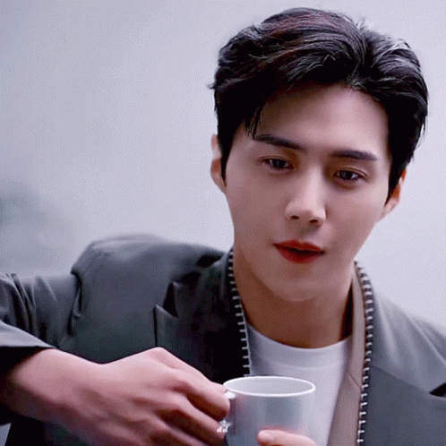 A Man In A Suit Is Holding A White Cup GIF