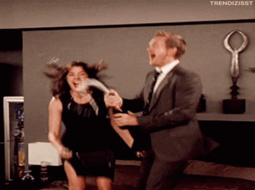 A Man In A Suit Is Holding A Woman In A Black Dress Who Is Laughing GIF