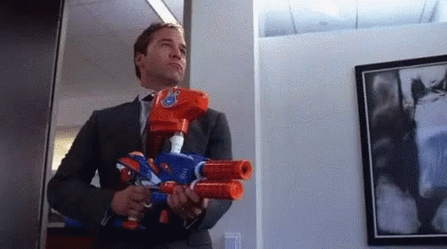 A Man In A Suit Is Holding Two Nerf Guns . GIF