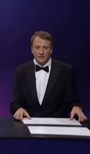 A Man In A Suit Is Holding Up A Sign That Says Tony Hawk GIF