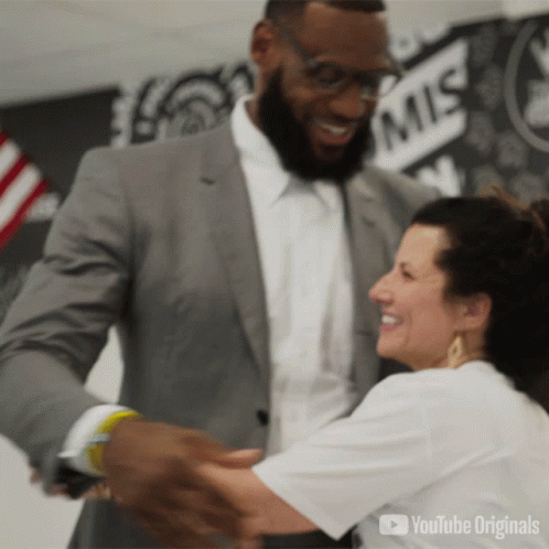 A Man In A Suit Is Hugging A Woman In Front Of A Wall That Says Mis GIF