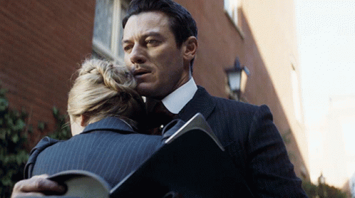 A Man In A Suit Is Hugging A Woman Who Is Holding A Folder GIF