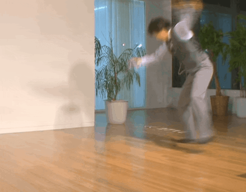 A Man In A Suit Is Jumping In A Room With A Plant In A Pot GIF