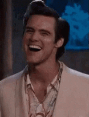 A Man In A Suit Is Laughing And Looking At The Camera . GIF