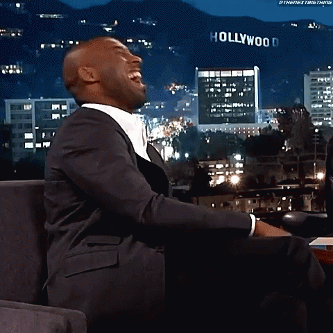 a man in a suit is laughing in front of a sign that says hollywood