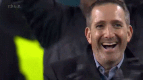 A Man In A Suit Is Laughing While Sitting In The Stands . GIF