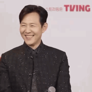 A Man In A Suit Is Laughing With His Eyes Closed And His Hands In The Air . GIF