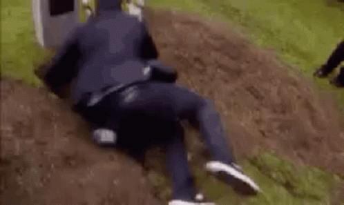 A Man In A Suit Is Laying In The Dirt In Front Of A Grave . GIF