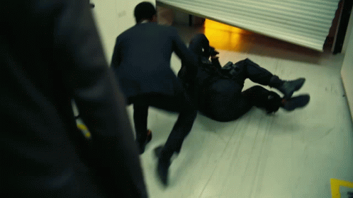 A Man In A Suit Is Laying On The Floor While Another Man Stands Behind Him GIF