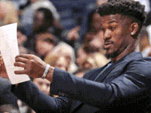 A Man In A Suit Is Looking At A Piece Of Paper . GIF