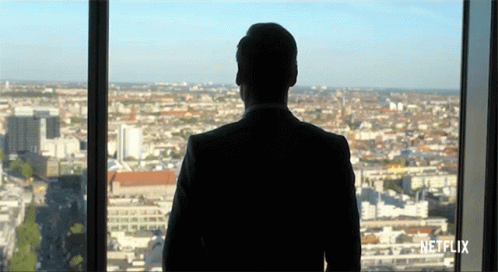 A Man In A Suit Is Looking Out Of A Window With Netflix Written On The Bottom GIF