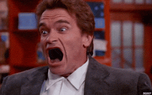A Man In A Suit Is Making A Funny Face With His Mouth Wide Open . GIF