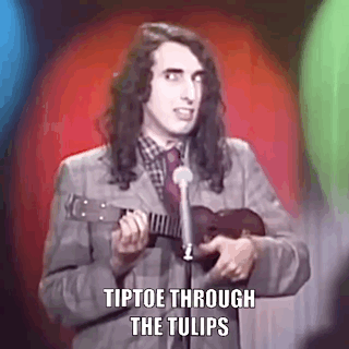 A Man In A Suit Is Playing An Ukulele In Front Of A Microphone . GIF