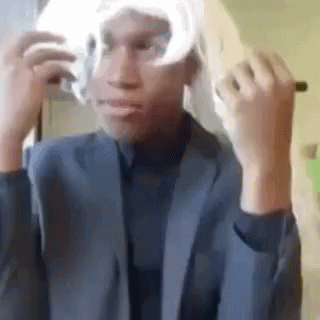 A Man In A Suit Is Putting On A Wig . GIF