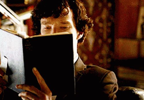 A Man In A Suit Is Reading A Book With The Word Sherlock Written On The Cover GIF