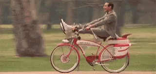 A Man In A Suit Is Riding A Bicycle With His Feet Up In A Park . GIF