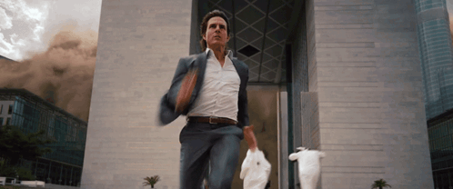 A Man In A Suit Is Running In Front Of A Building GIF