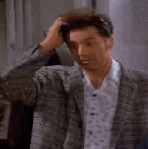 A Man In A Suit Is Scratching His Head While Standing In A Room . GIF