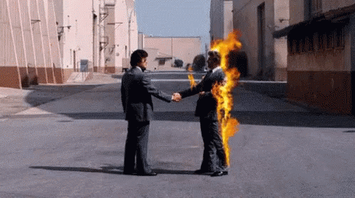 A Man In A Suit Is Shaking Hands With Another Man In A Suit Who Is On Fire . GIF