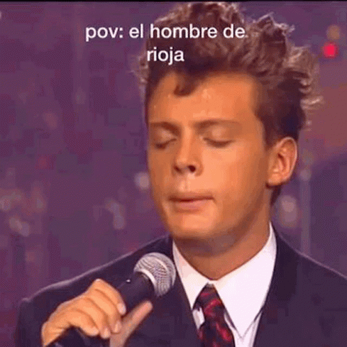 A Man In A Suit Is Singing Into A Microphone . GIF