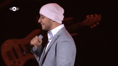 A Man In A Suit Is Singing Into A Microphone While Wearing A White Beanie GIF