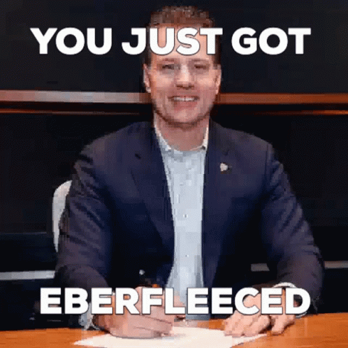 A Man In A Suit Is Sitting At A Desk With A Sign That Says `` You Just Got Ebfleeced '' . GIF