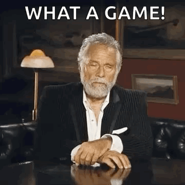 A Man In A Suit Is Sitting At A Table Covering His Face With His Hand And Making A Funny Face . GIF