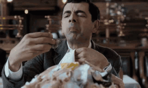 A Man In A Suit Is Sitting At A Table Eating A Large Amount Of Food . GIF