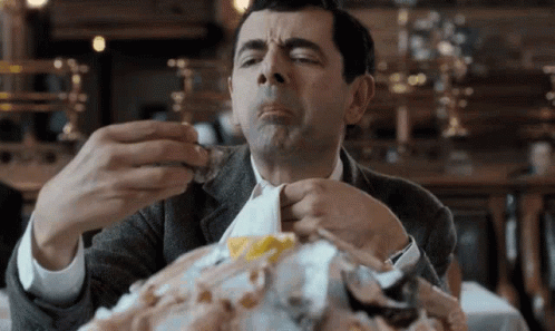 A Man In A Suit Is Sitting At A Table Eating A Large Amount Of Food . GIF