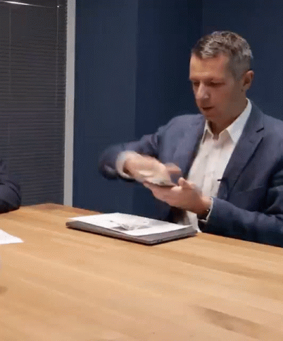 A Man In A Suit Is Sitting At A Table With A Laptop GIF