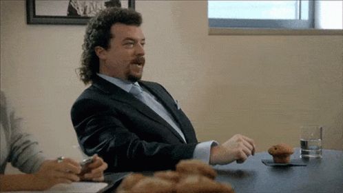 A Man In A Suit Is Sitting At A Table With A Muffin On It GIF